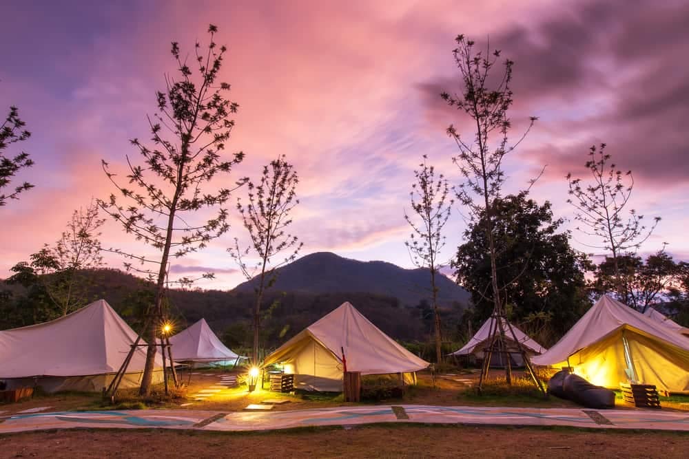 A group of glamping tents lit up at dusk with mountains in the background.