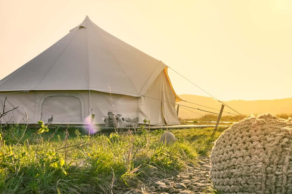 A white tent sits on a grassy field at sunset, offering a picturesque spot for glamping enthusiasts.