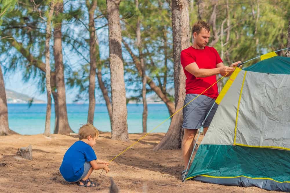 A man and a boy setting up a tent at a campground on the beach.