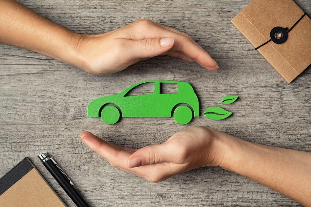A pair of hands gently cradling a vibrant green car on a polished wooden table.