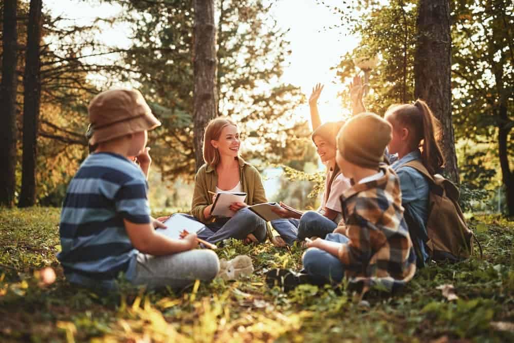 A group of children sitting on the ground in the woods, participating in a nature program that promotes Nevada State Parks.