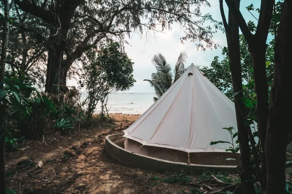 A white tent sits on the beach next to trees at a LeadingCampings site in Europe.