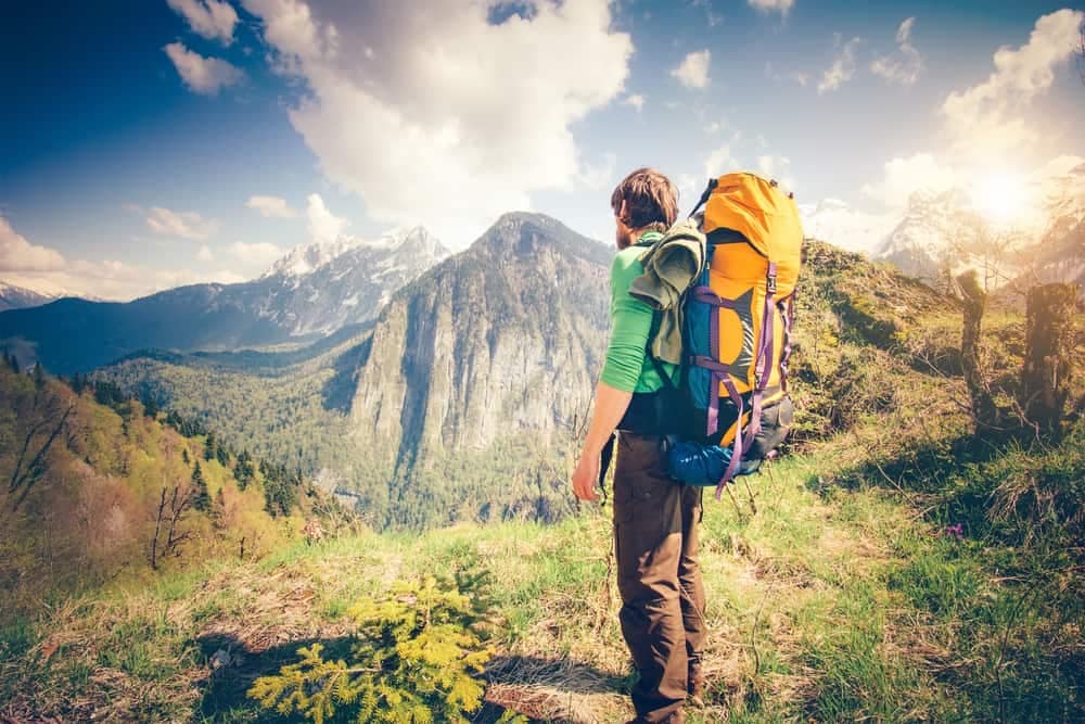 A man with a backpack is celebrating as he looks at the mountains.