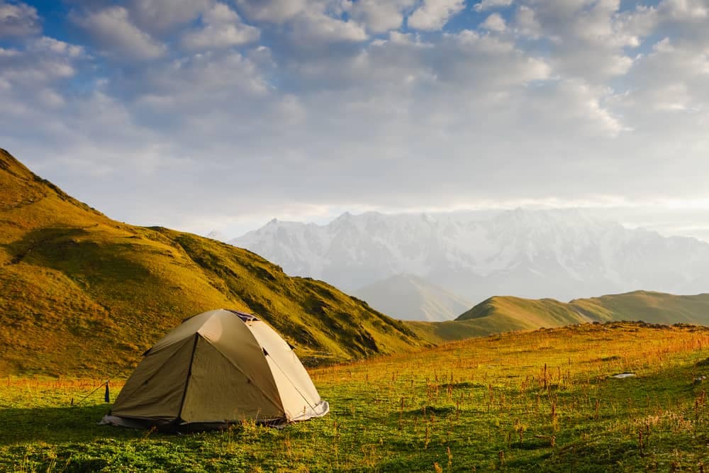 A tent pitched in a grassy field with mountains in the background. The perfect scene for a serene camping experience in Europe with LeadingCampings.