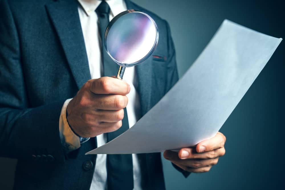 A man in a suit holding a magnifying glass inspects an RV.