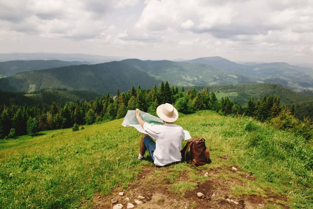A woman is sitting on a hill looking at a Campspot map for the Top 10 Campgrounds in America Annual Awards Program.