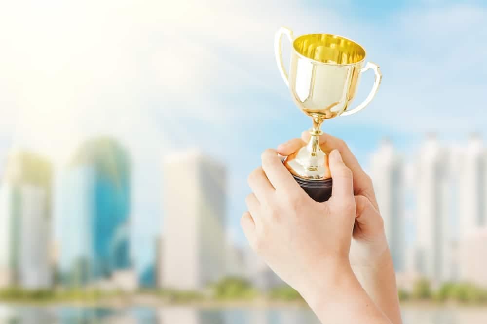 A hand holding a gold trophy representing the 2023 COHCE Award Nominations criteria, set against the backdrop of a city.