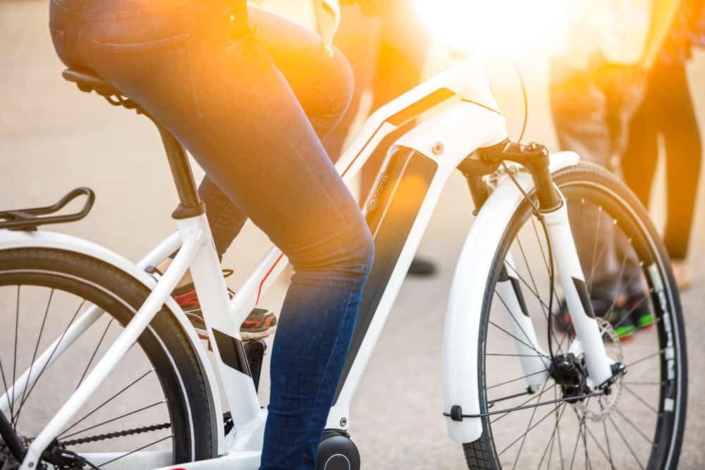 A woman is riding a Denago electric bike in the sun, catering to RV & Van Life enthusiasts.