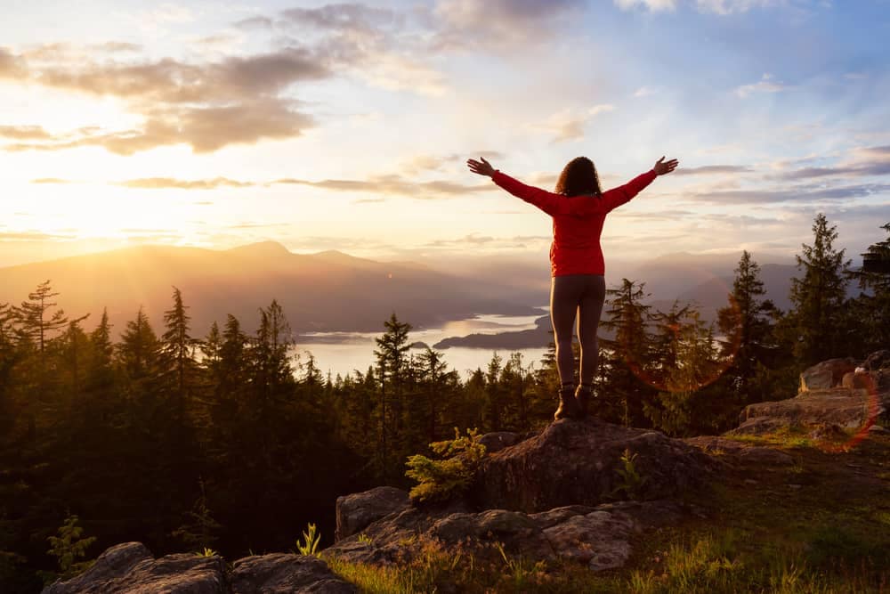 A woman standing on top of Cape Roger Curtis Park with her arms outstretched, enjoying the breathtaking views of Metro Vancouver.