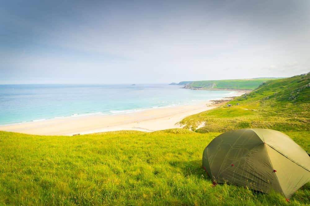 A tent sits on top of a grassy hill overlooking a beach in Gwynedd, Wales.
