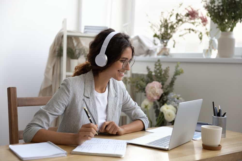 A woman wearing headphones and sitting at a desk with a laptop, participating in the Canadian Outdoor Hospitality Conference alongside industry experts.