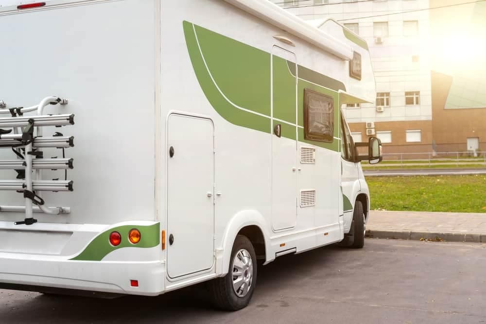 A white and green RV parked in front of the City of Quesnel building.