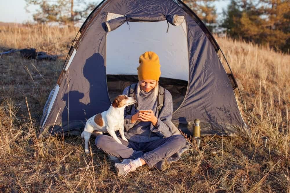 A woman sits in front of a tent with her dog, enjoying an Enhanced Outdoor Experience provided by Parks Canada.