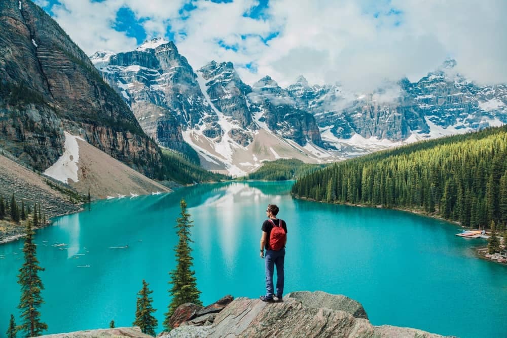 A man standing on a rock overlooking a lake in Banff National Park, showcasing Canada's thriving tourism industry.