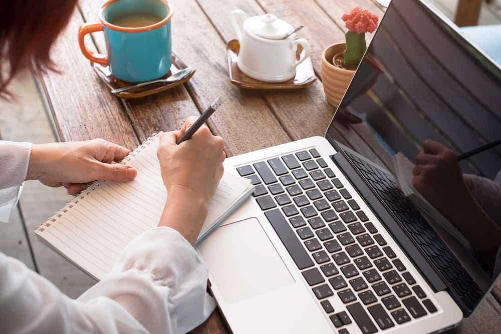 Top Industry Expert, KOA's O'Rourke, attending 2023 Canadian Outdoor Hospitality Conference and writing on a notebook while sitting at a table with a cup of coffee.