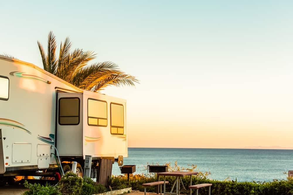 A private-owned RV parked on the California beach at sunset, navigating regulatory hurdles.