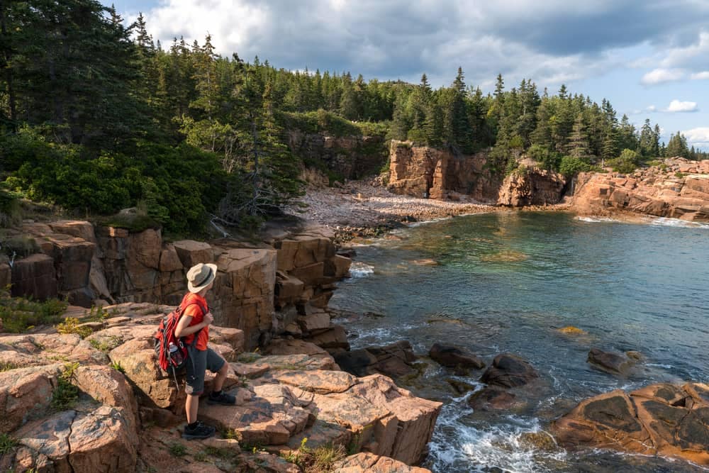 A man is standing on a rocky cliff overlooking the ocean in Acadia National Park during the shoulder season.