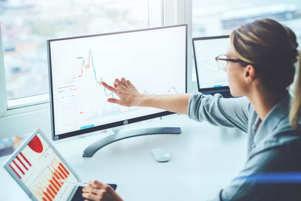 A Financial Analyst from IVEE Group is pointing at a graph on a computer screen in a team meeting.