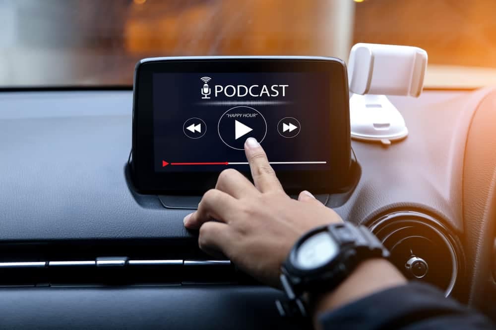 A person is pointing at a device in a car that has a podcast on it, showcasing the benefits of Campground Marketing Success.