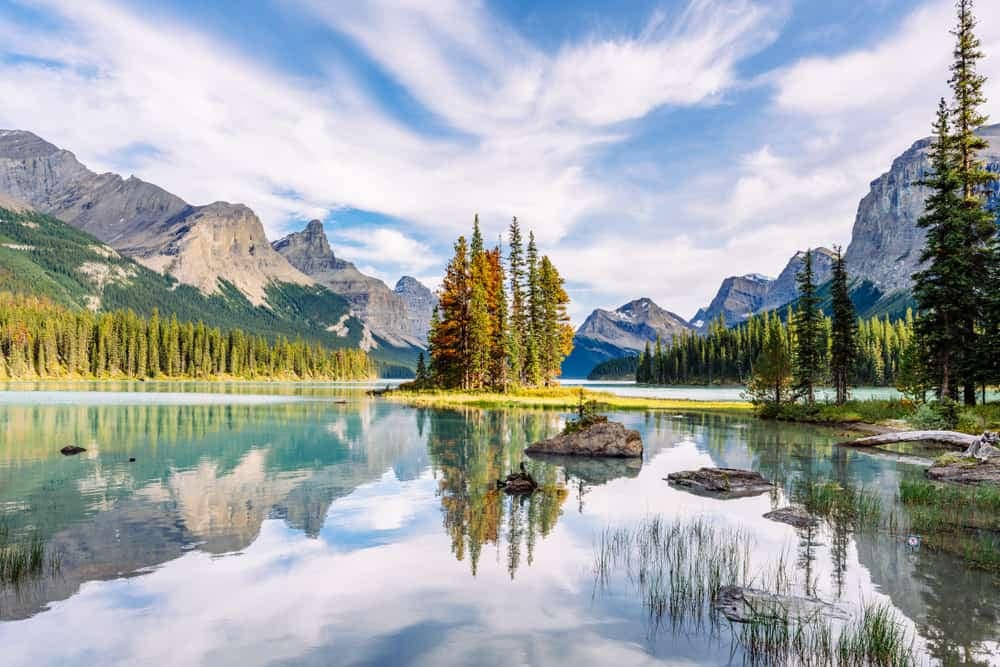 A serene lake nestled amidst picturesque mountains and lush green trees, harmoniously blending with the surrounding natural landscape.