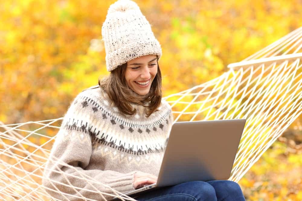 A woman sitting in a hammock browsing the internet on her laptop, enjoying the benefits of AGA Partners' insider perks and utilizing free websites.
