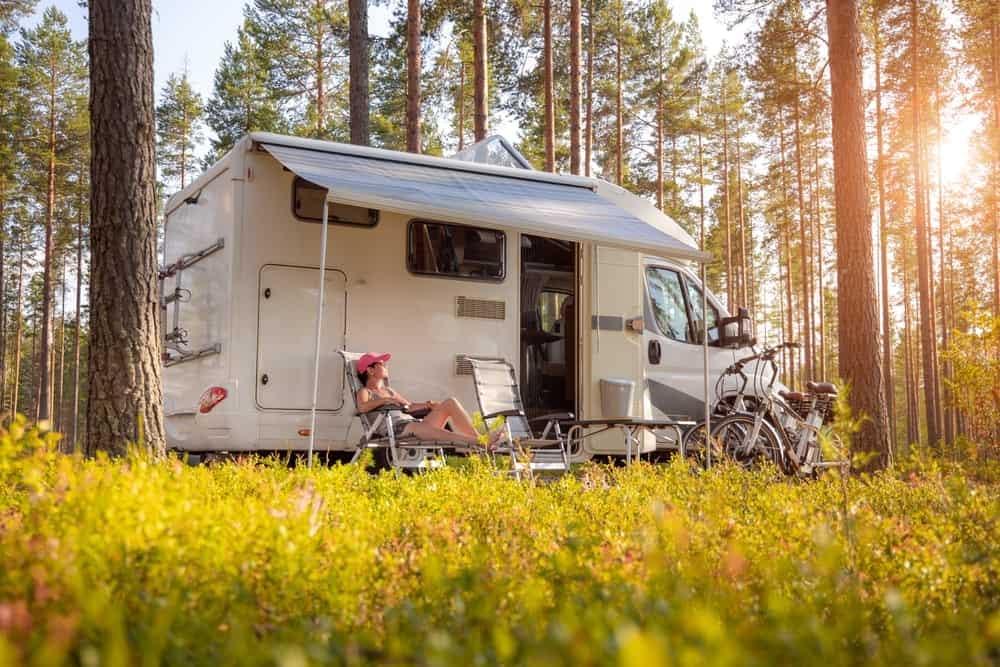 A woman sits in front of an RV, immersed in the serene beauty of the outdoors.