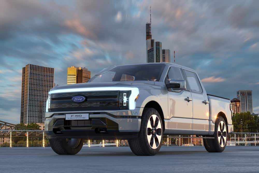 A silver Ford F-150 pickup truck is parked in front of a city.