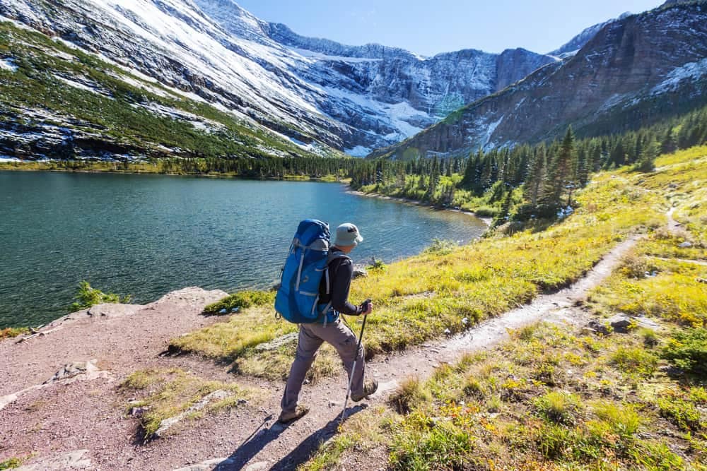 A hiker walking along a trail near a lake in Glacier National Park.