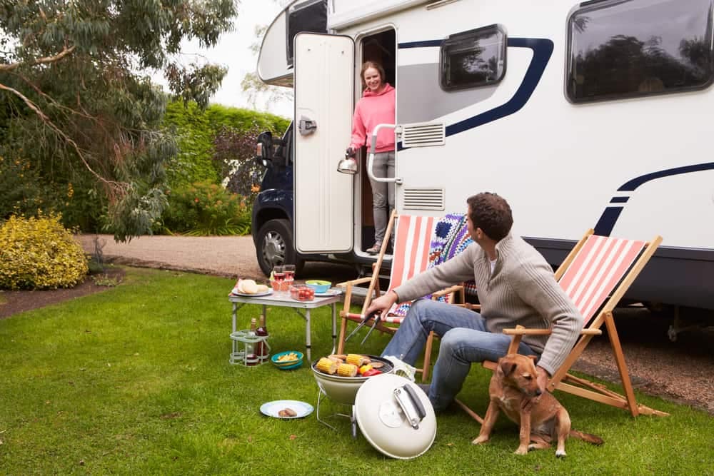 Increased occupancy at a campground as a man and woman sit in lawn chairs next to an RV with their dog.