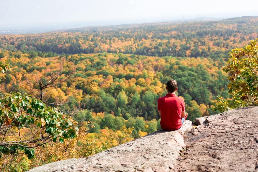 A man sitting on top of a rock overlooking Gatineau Park.