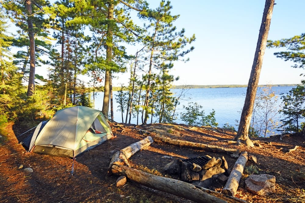 A sustainable camping tent set up in the woods near a lake, offering an authentic Indigenous Tourism Ontario experience.