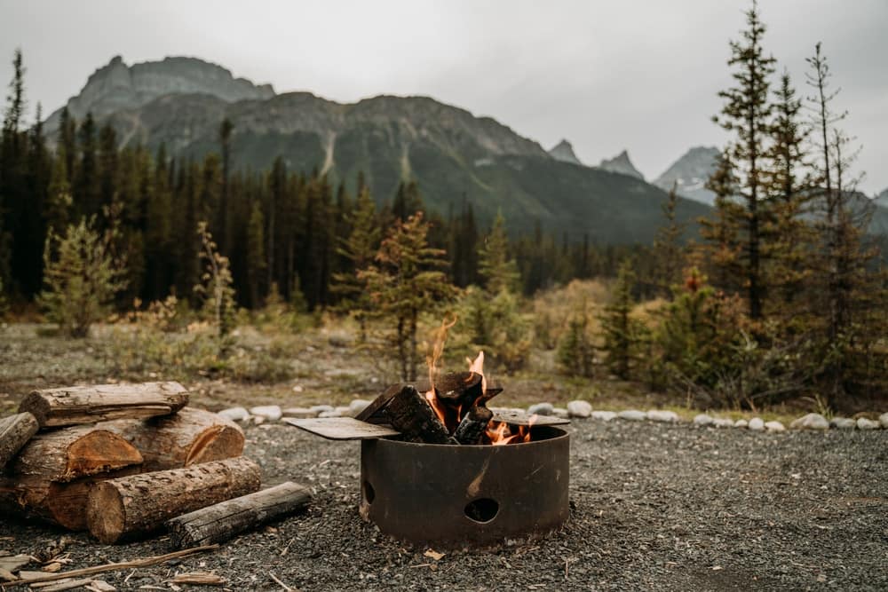 A camping fire pit in the middle of a field with mountains in the background.