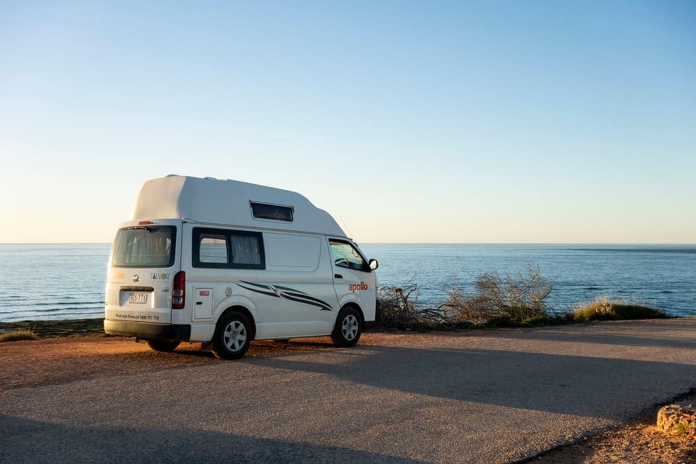 A white camper van parked on the side of a road near the ocean in Exmouth.