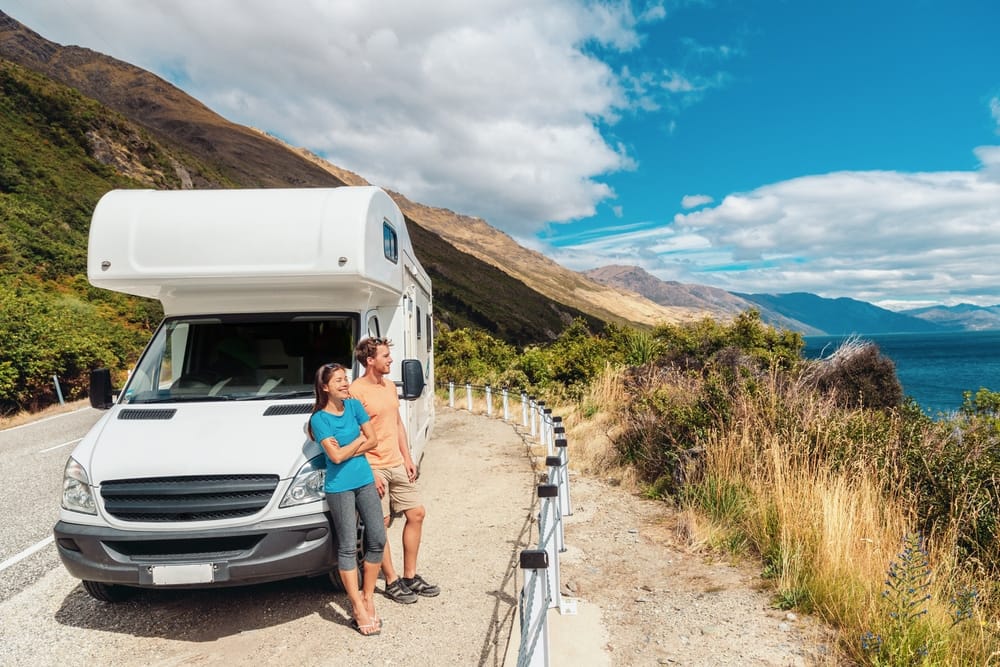 A couple standing next to a white RV in front of a lake, enjoying their Sun Communities experience in Q1 2023 and being pleasantly surprised by the exceeded expectations.