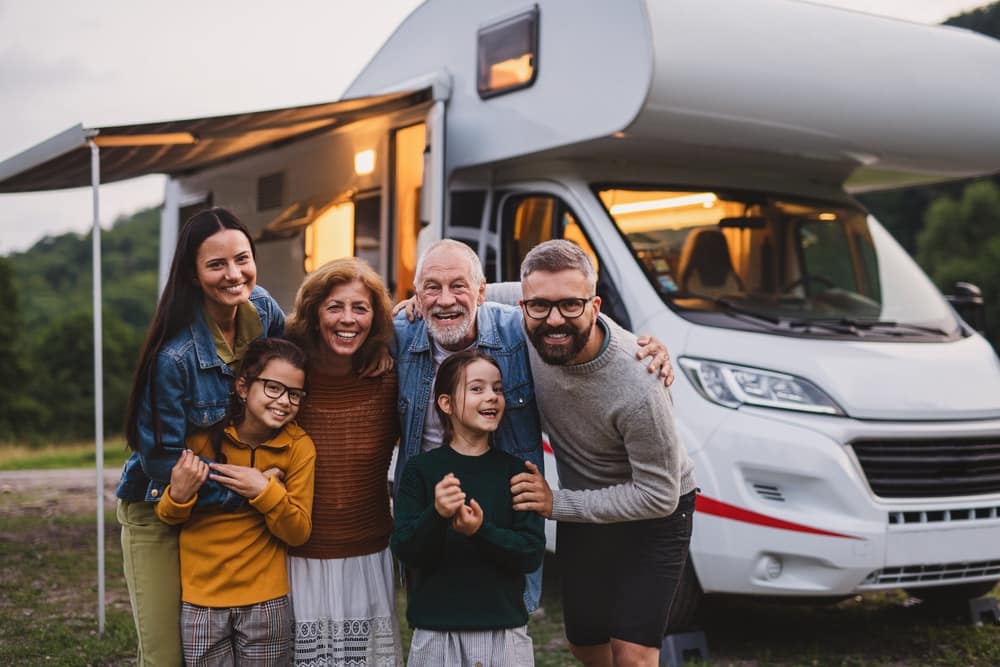 A enthusiastic family posing in front of an RV during a camping trip on Memorial Day.
