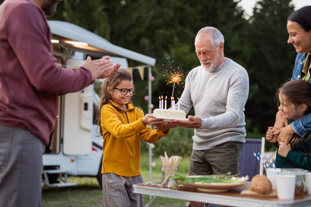 A group of enthusiastic people celebrating a birthday while camping in front of an RV.