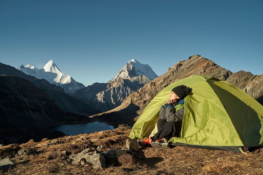 A man sits in front of a tent amidst the majestic mountains of China, taking in the breathtaking scenery during the May Day Holiday.