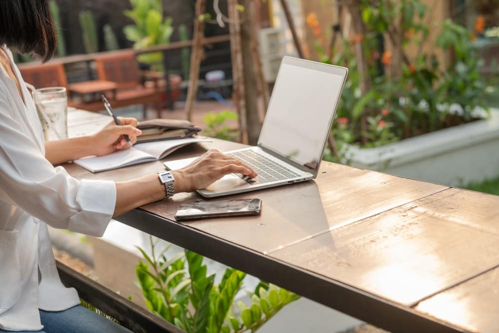 A woman working on her laptop at a table in an outdoor garden.