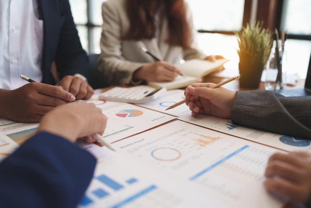 A group of business people, including the Director of Finance, David Model, sitting around a table with papers and graphs.