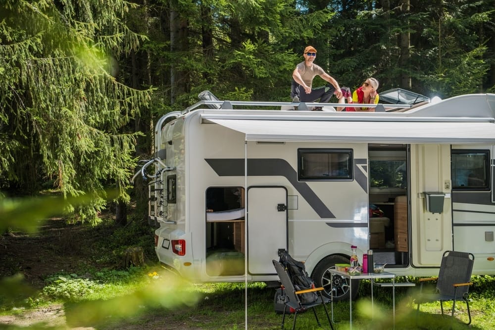 Two people standing on top of an RV in the woods, celebrating Sun Communities' Q1 2023 Results that Exceeded Expectations.