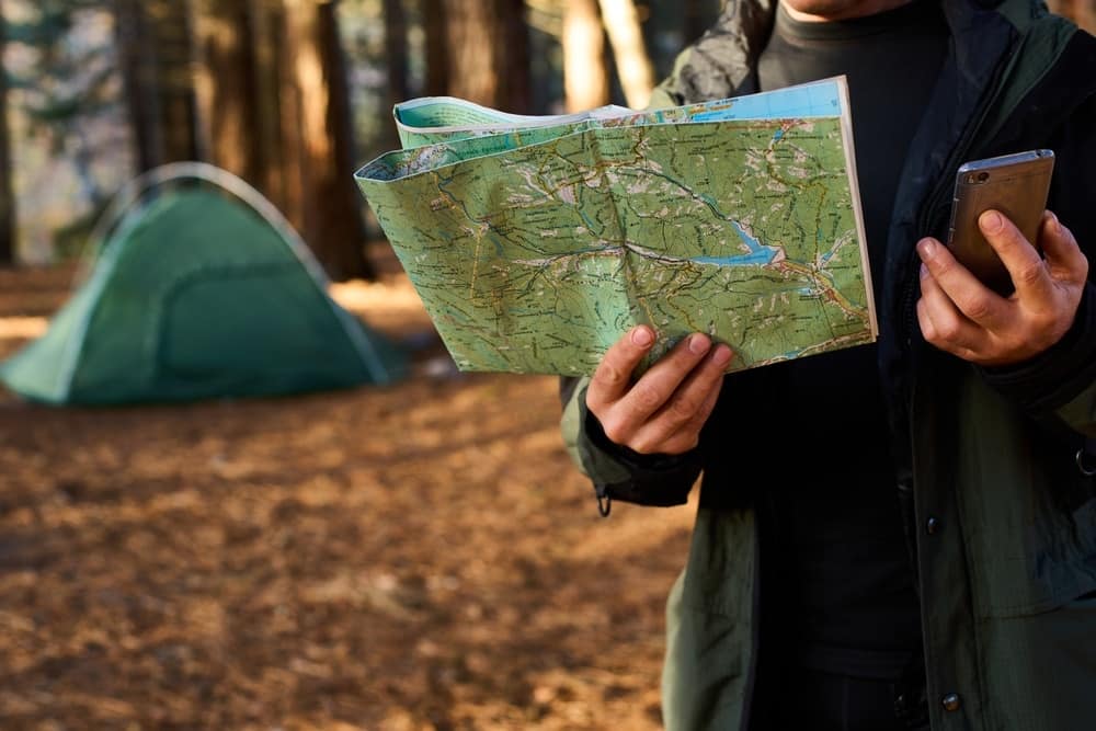 A man holding a map in front of a tent, embarking on an Outdoor Adventure.