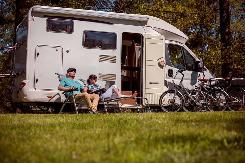 Two people sitting in front of an RV, celebrating National Go RVing Day.