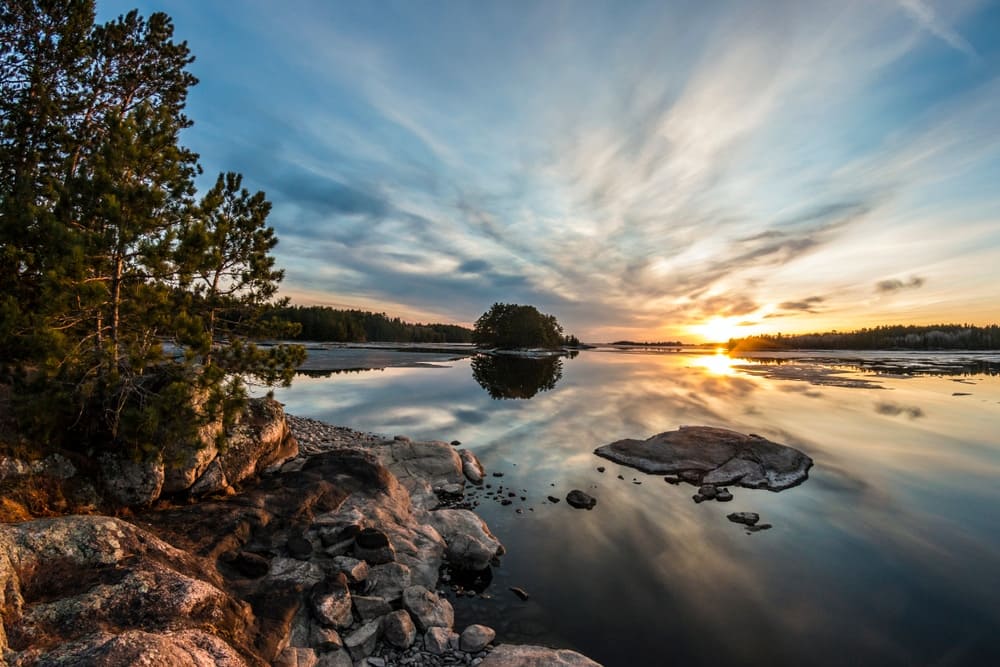 Camp at The Dyrt 2023 Best Places with the sun setting over a lake, rocks, and trees.