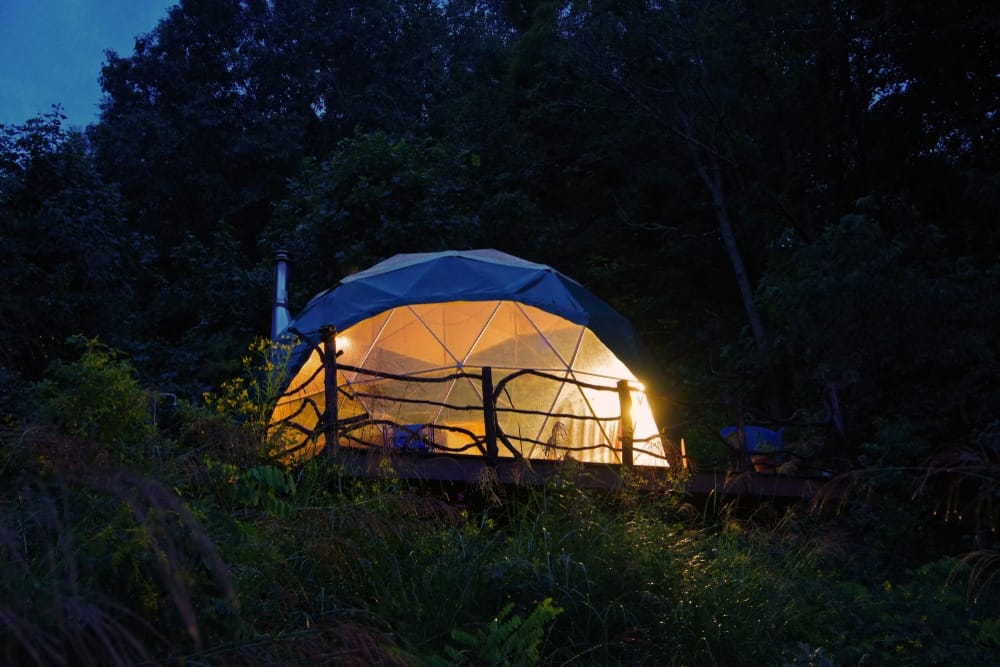 A tent lit up at night in a wooded area, part of Lamoine's proposed glamping resort.