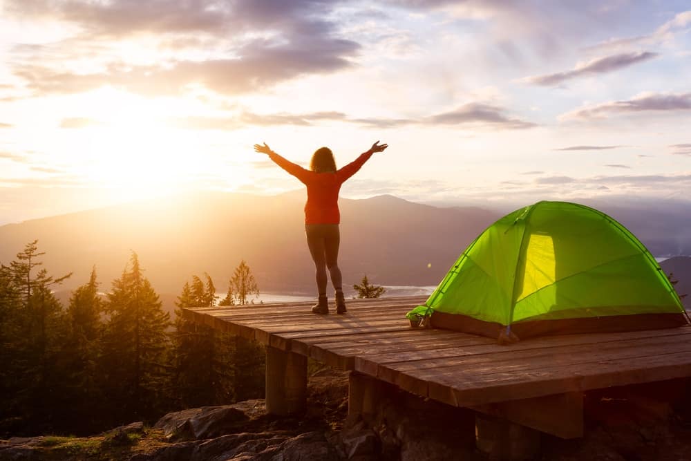 A woman standing in front of a tent at sunset during her BC Camping Trip.