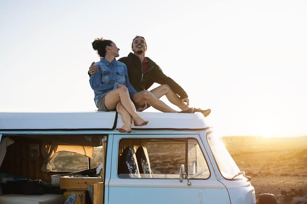 Couple enjoying camping season on top of a van at sunset.