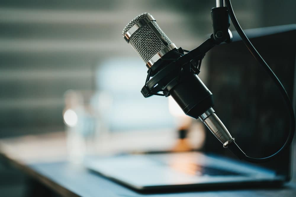A microphone sits on a desk next to a laptop as Joel Holland, the CEO and founder of Harvest Hosts, shares his success story.