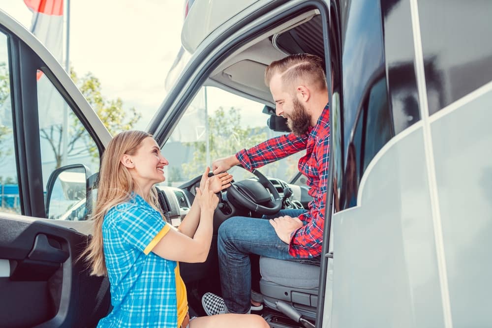 A man and a woman are sitting in the door of a camper van, taking part in the revamping of their RV buying experience.