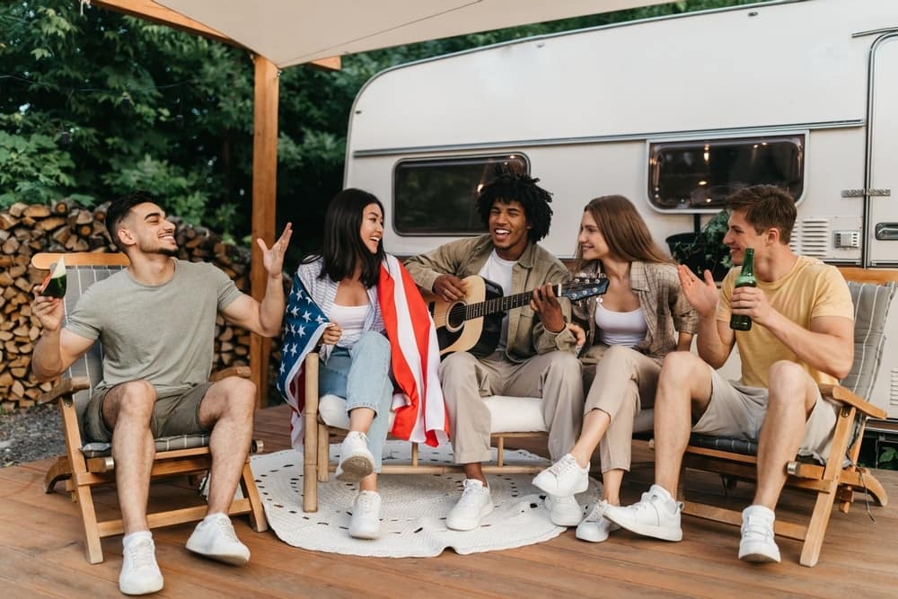 A group of friends sitting on the porch of an RV enjoying the Camping Season.