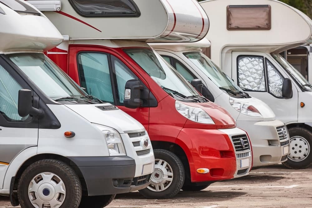 A row of affordable RVs parked in a parking lot.